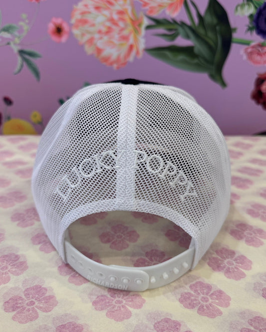 A white mesh baseball cap with a white adjustable strap, shown on a patterned surface with a floral background.